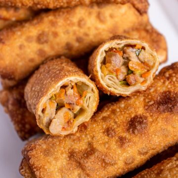 Closeup of a halved egg roll on top of a pile of more egg rolls.