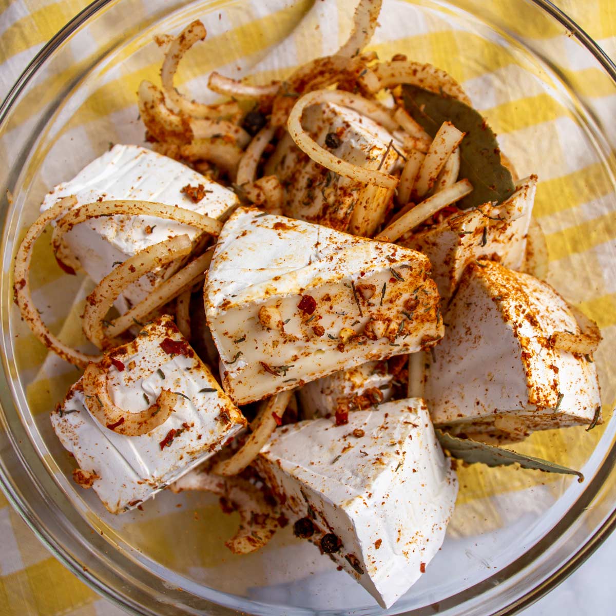 Wedges of brie cheese tossed with spices and sliced onions in a glass bowl.