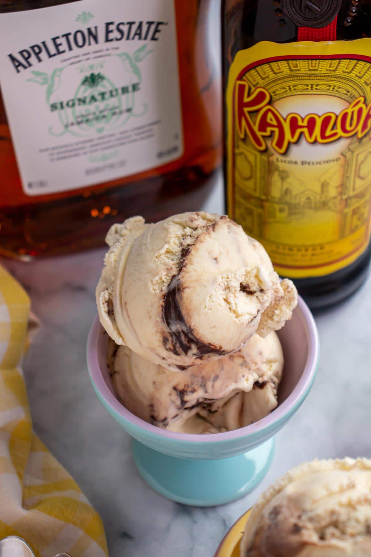 Two scoops of ice cream in a blue ceramic dish with alcohol bottles in the background.