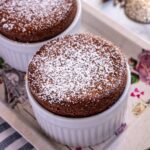 Two chocolate soufflés dusted with powdered sugar on a small decorative tray.