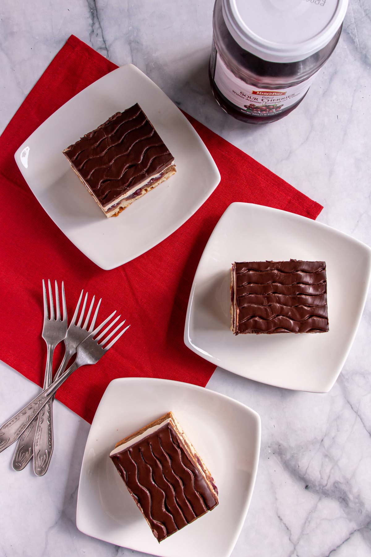 Three rectangular slices of cake with chocolate glaze on white square plates.