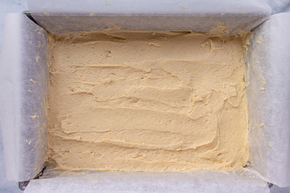 Thick vanilla cake batter spread into a parchment paper lined rectangular cake pan.