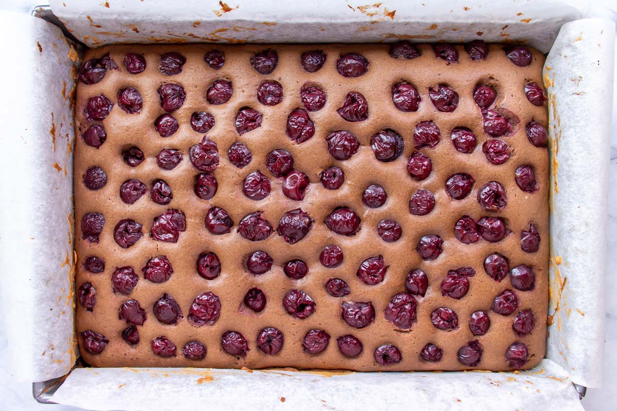 A rectangular chocolate cake with rows of cherries baked into the top.