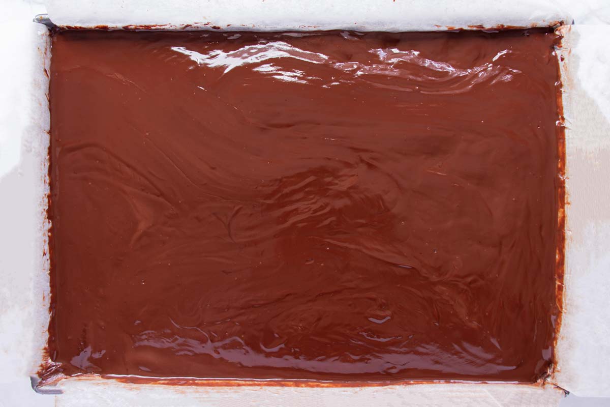 Chocolate ganache spread over the top of a cake in a rectangular pan.
