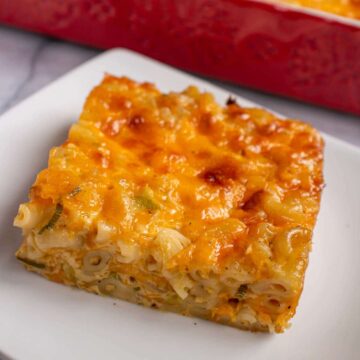A square piece of macaroni pie on a plate with a red dish in the background.