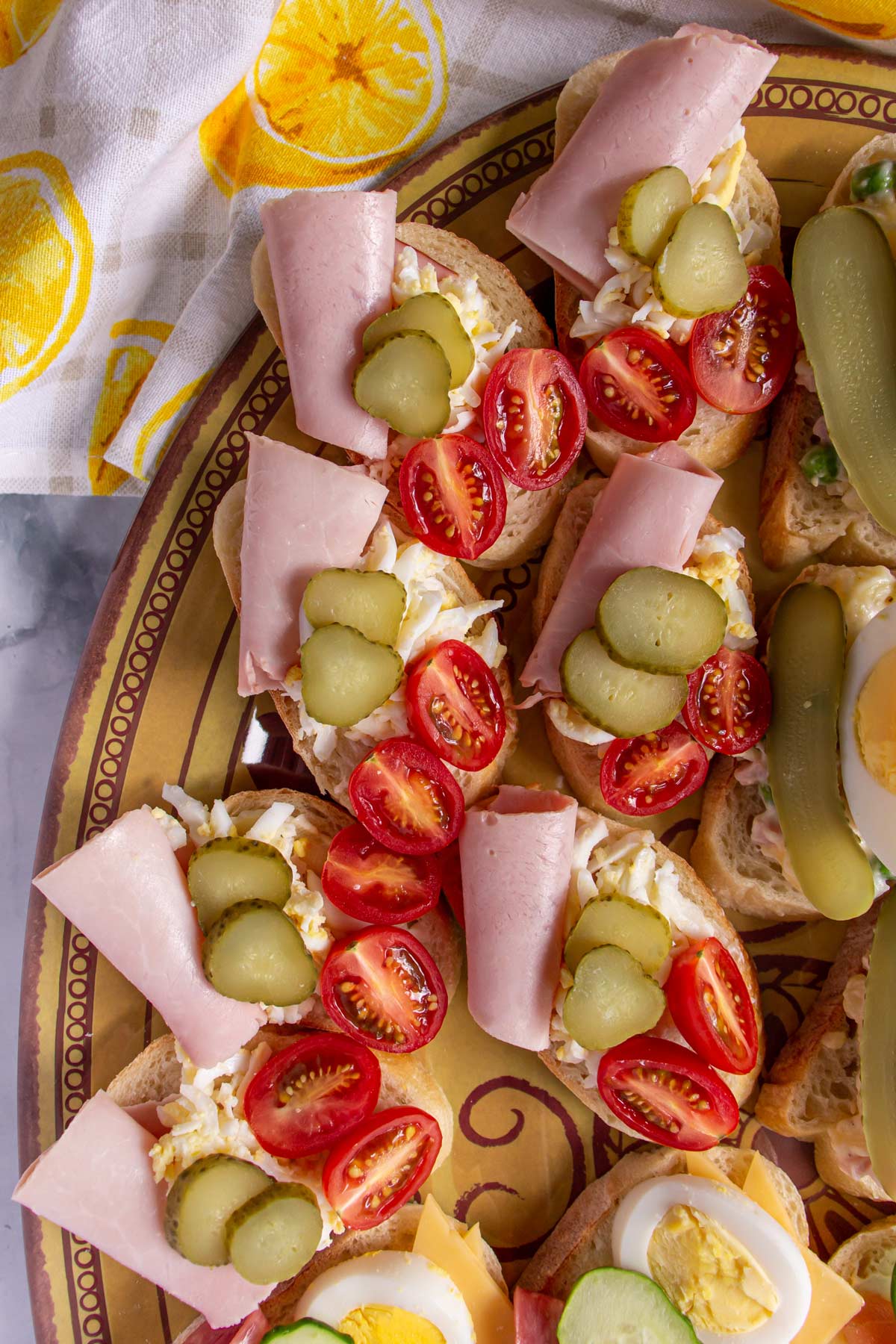 Open-faced sandwiches topped with ham, halved cherries tomato, and sliced pickle.