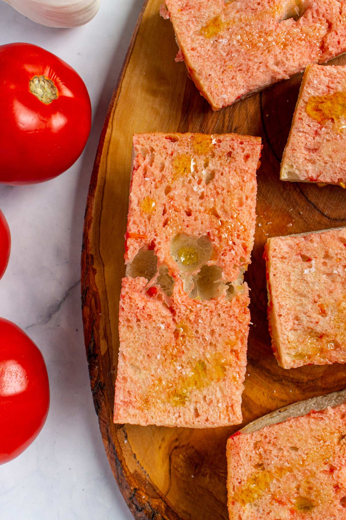 Closeup of Spanish tomato bread drizzled with olive oil on a wooden board.