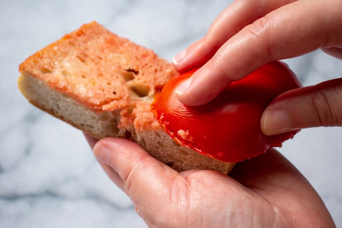 Closeup of a hand rubbing a halved tomato on a piece of bread.