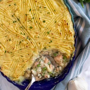 Fish pie in a blue oval baking dish with a spoon scooping some out.