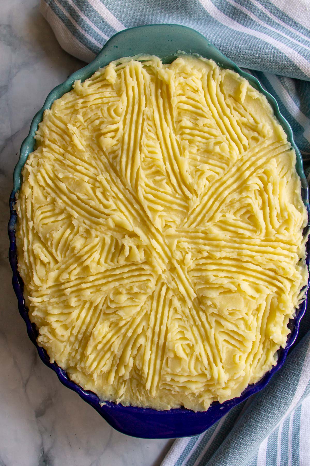 An unbaked mashed potato topped pie in a blue oval baking dish.