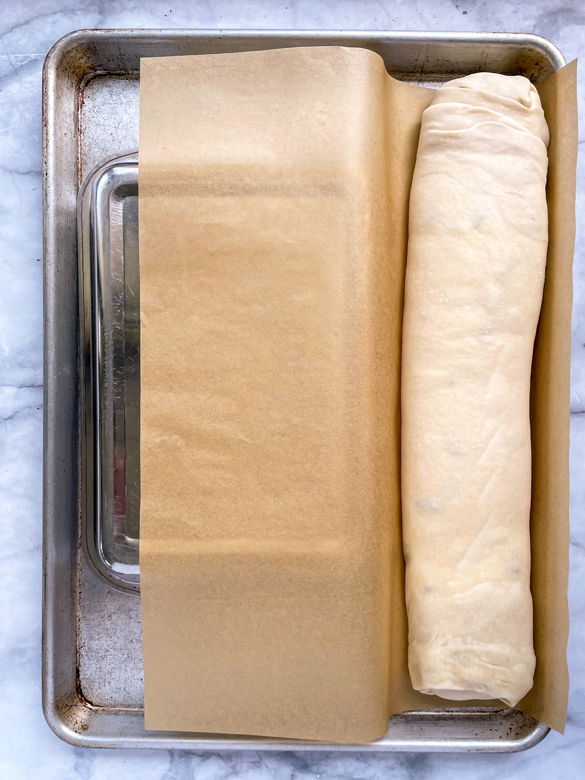 An unbaked strudel penned between the edge of a sheet pan and an inverted rectangular pan.