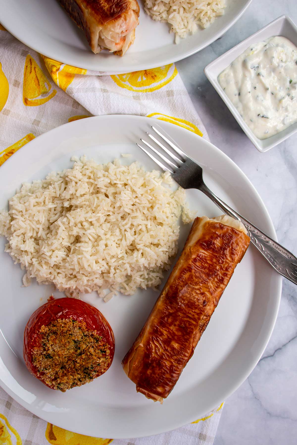 Salmon in phyllo, white rice, and a baked tomato on a white plate with a fork.