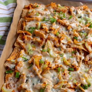 Buffalo chicken nachos with celery and scallions in rectangular pan with a striped towel next to it.