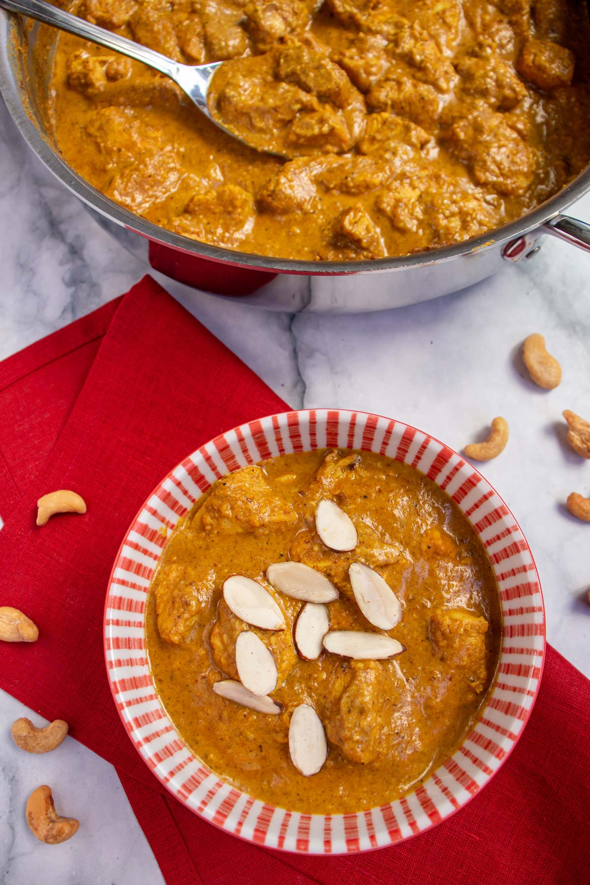 Chicken korma with sliced almonds in a red and white bowl on a red napkin.