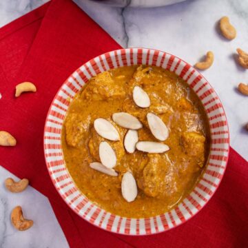 Chicken korma with sliced almonds in a red and white bowl on a red napkin.