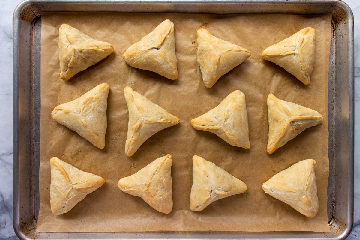 Baked triangular Lebanese spinach pies on a parchment paper lined baking sheet.