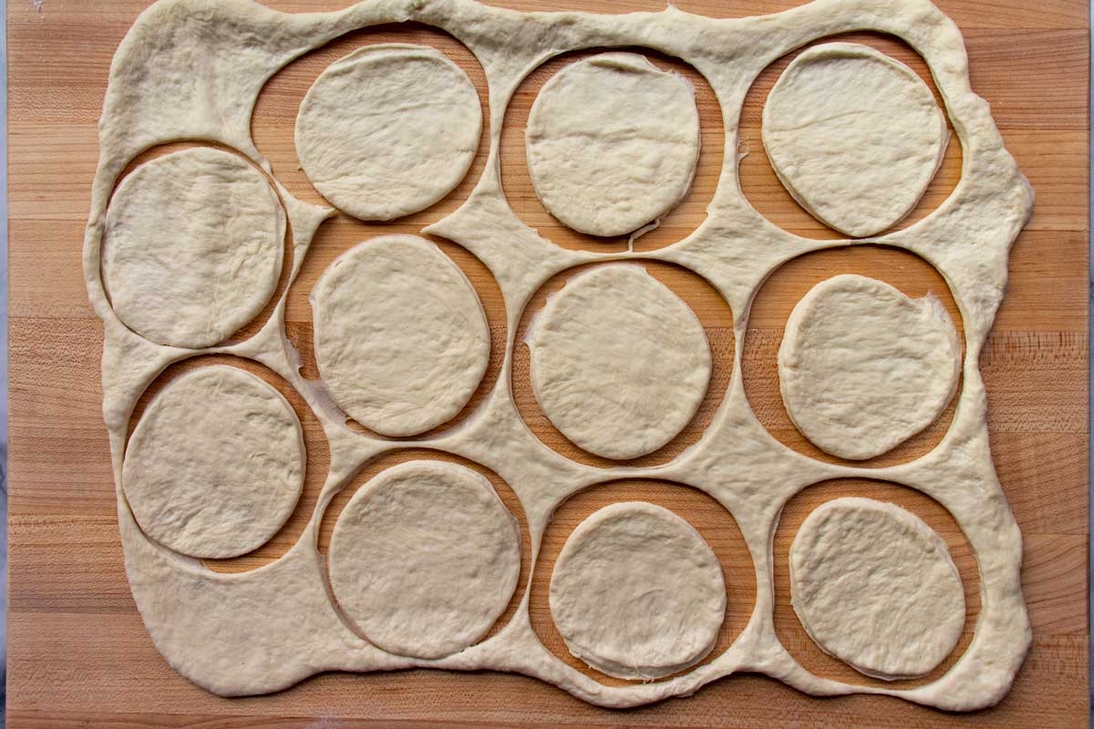 Circles cut out of a piece of rolled out dough on a wooden board.