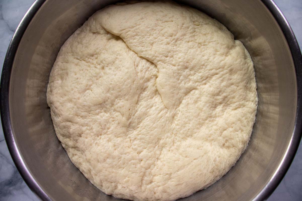 A ball of dough in a metal mixing bowl after proofing and doubling in size.
