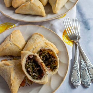 Triangular spinach pies on round plates with one cut open to show the filling.
