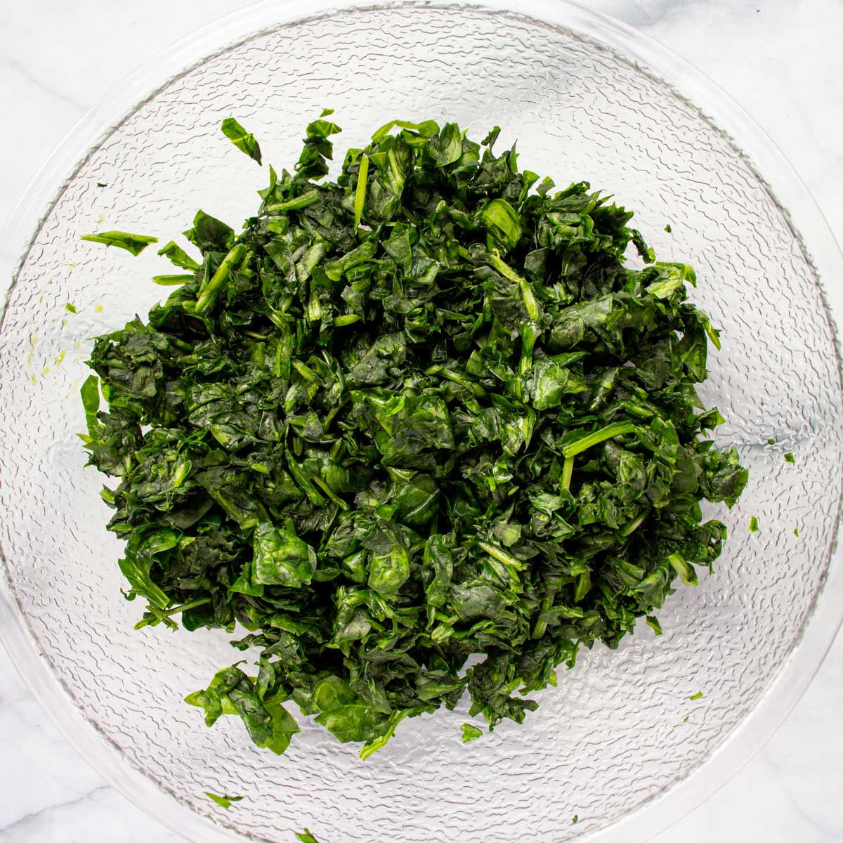 Wilted, squeezed-dry chopped spinach in a clear mixing bowl.
