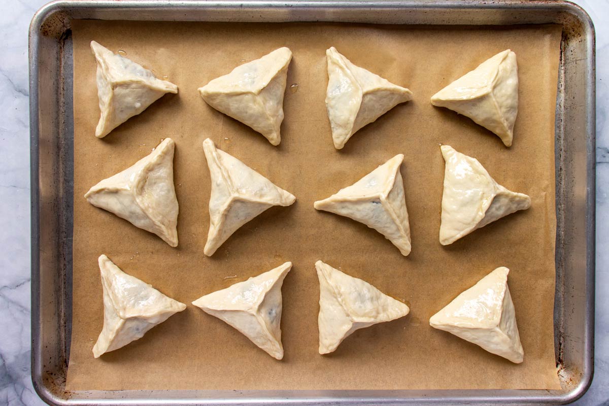 Unbaked triangular dough-wrapped spinach pies on a parchment paper lined baking sheet.