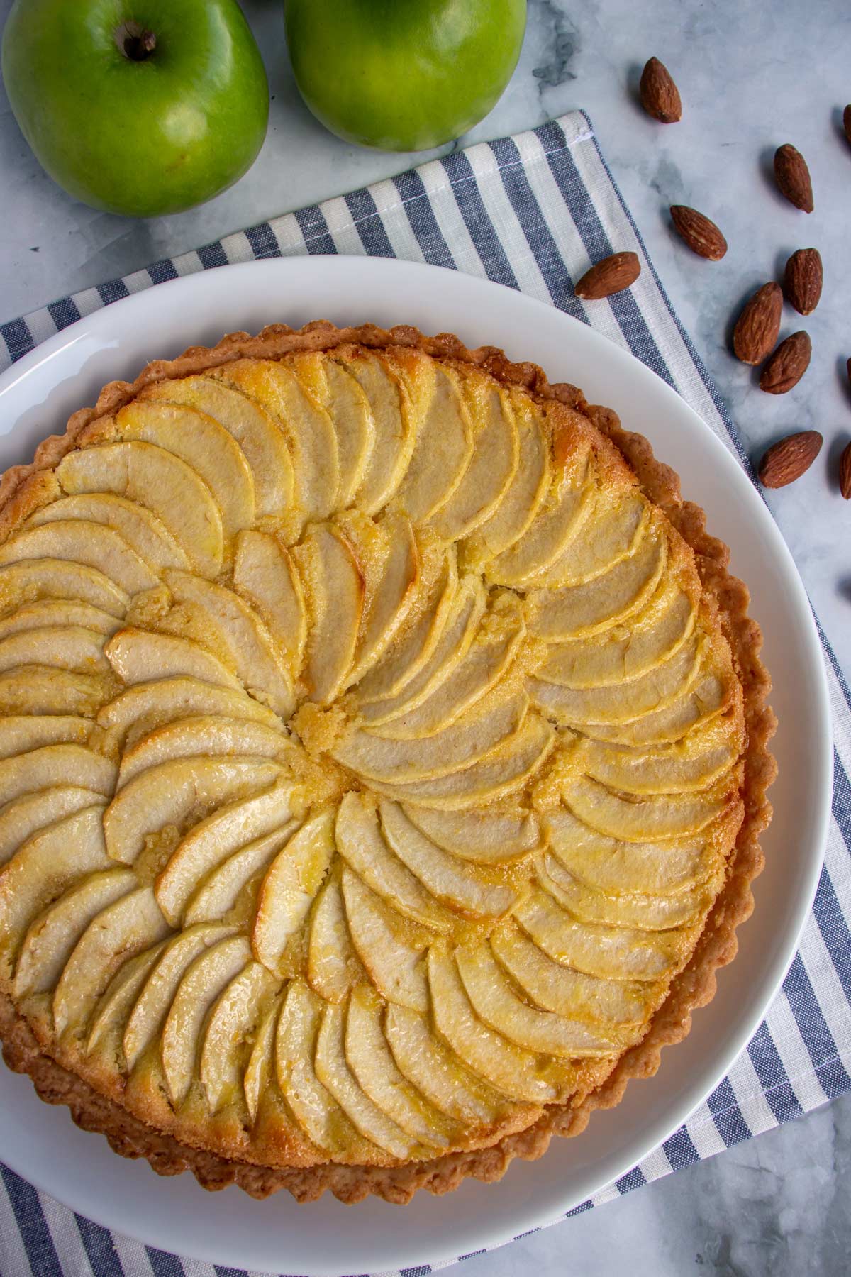 A French apple tart on a striped cloth napkin with almonds and apples.