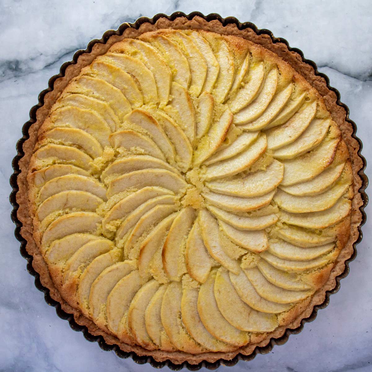 A baked tarte aux pommes (French apple tart) on a marble background.