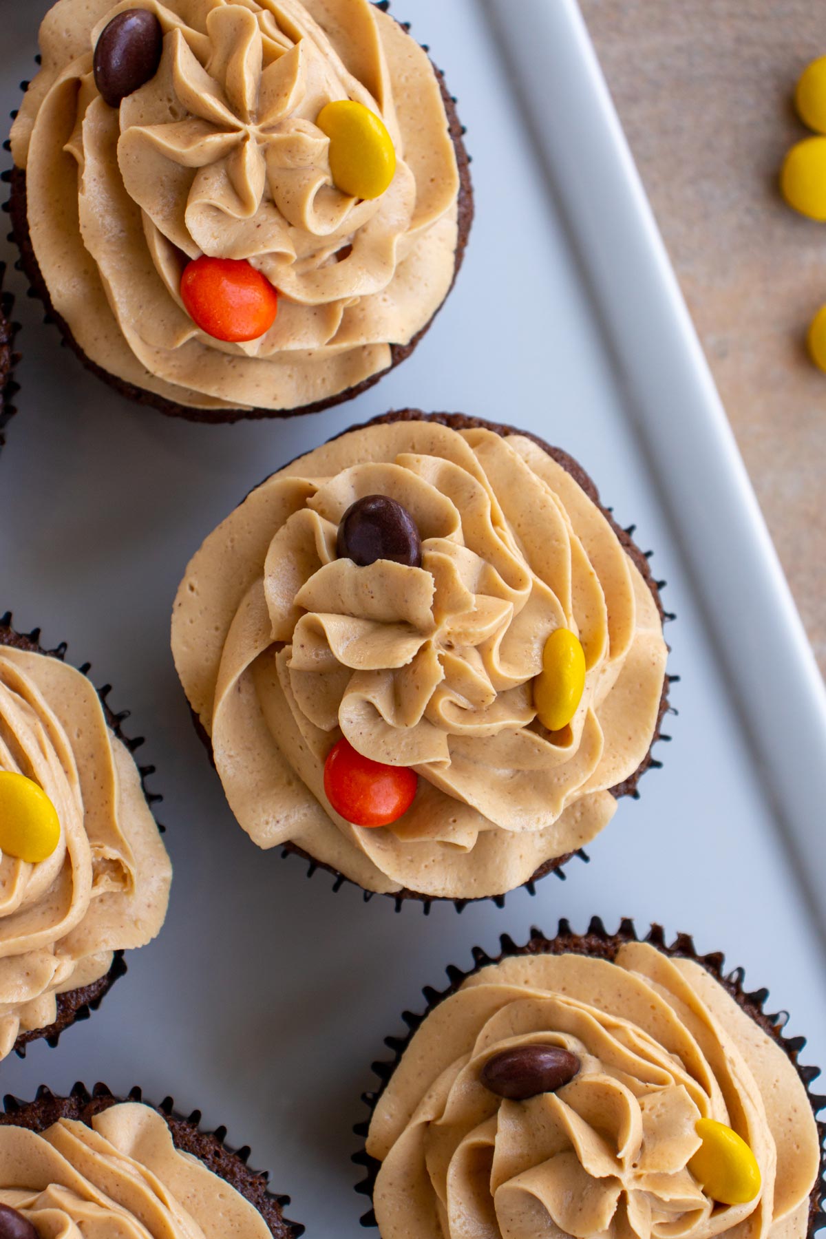 Peanut butter frosting piped on top of cupcakes with Reese's Pieces candies on top.