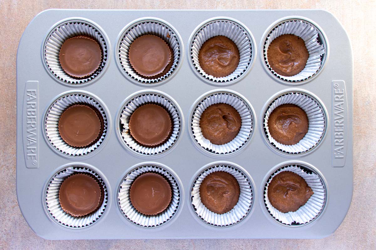 Assembling chocolate peanut butter cup cupcakes in a metal muffin pan.