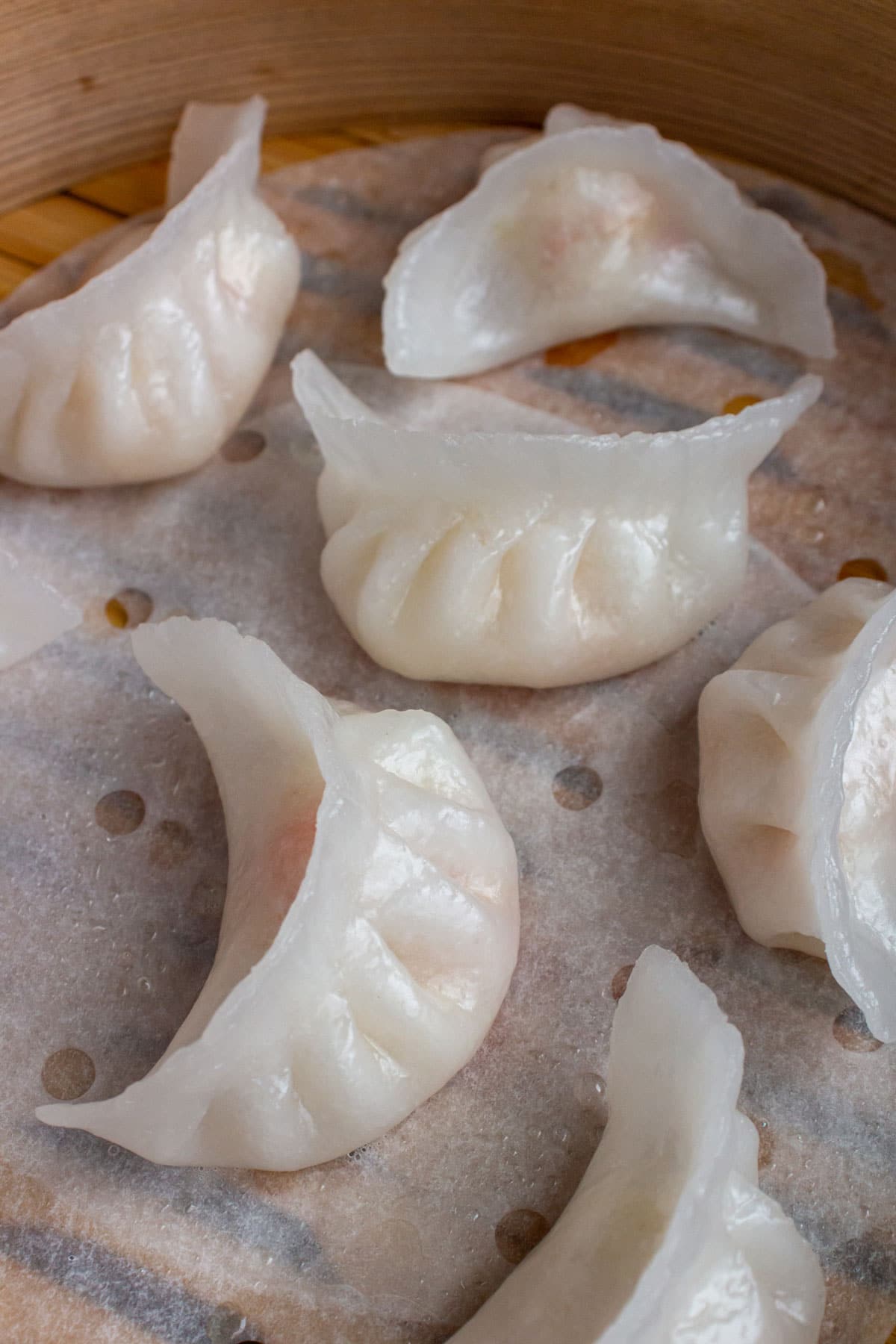 Closeup of white crystal shrimp dumplings with crescent shapes in a bamboo steamer basket.
