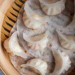 Translucent white crystal shrimp dumplings with crescent shapes in a bamboo steamer basket.