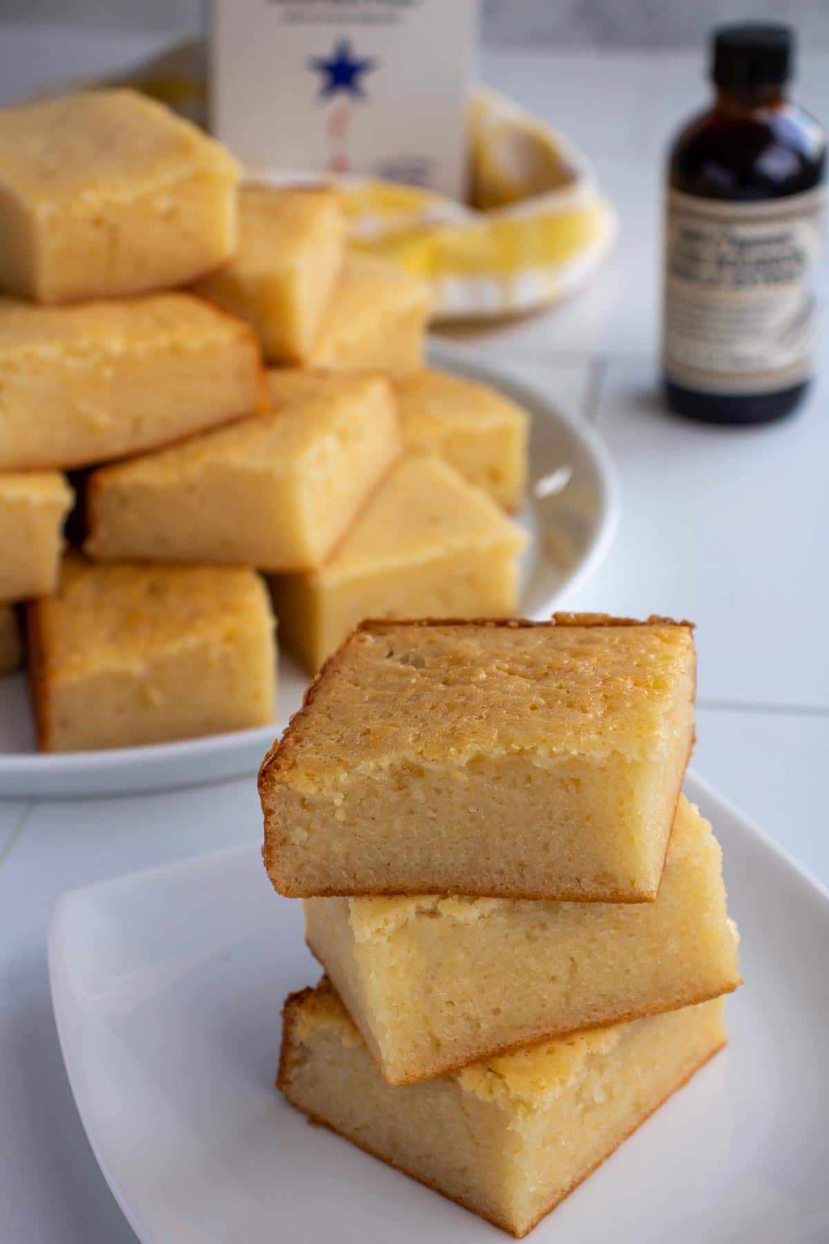 A stack of 3 butter mochi squares on a plate with a platter in the background.