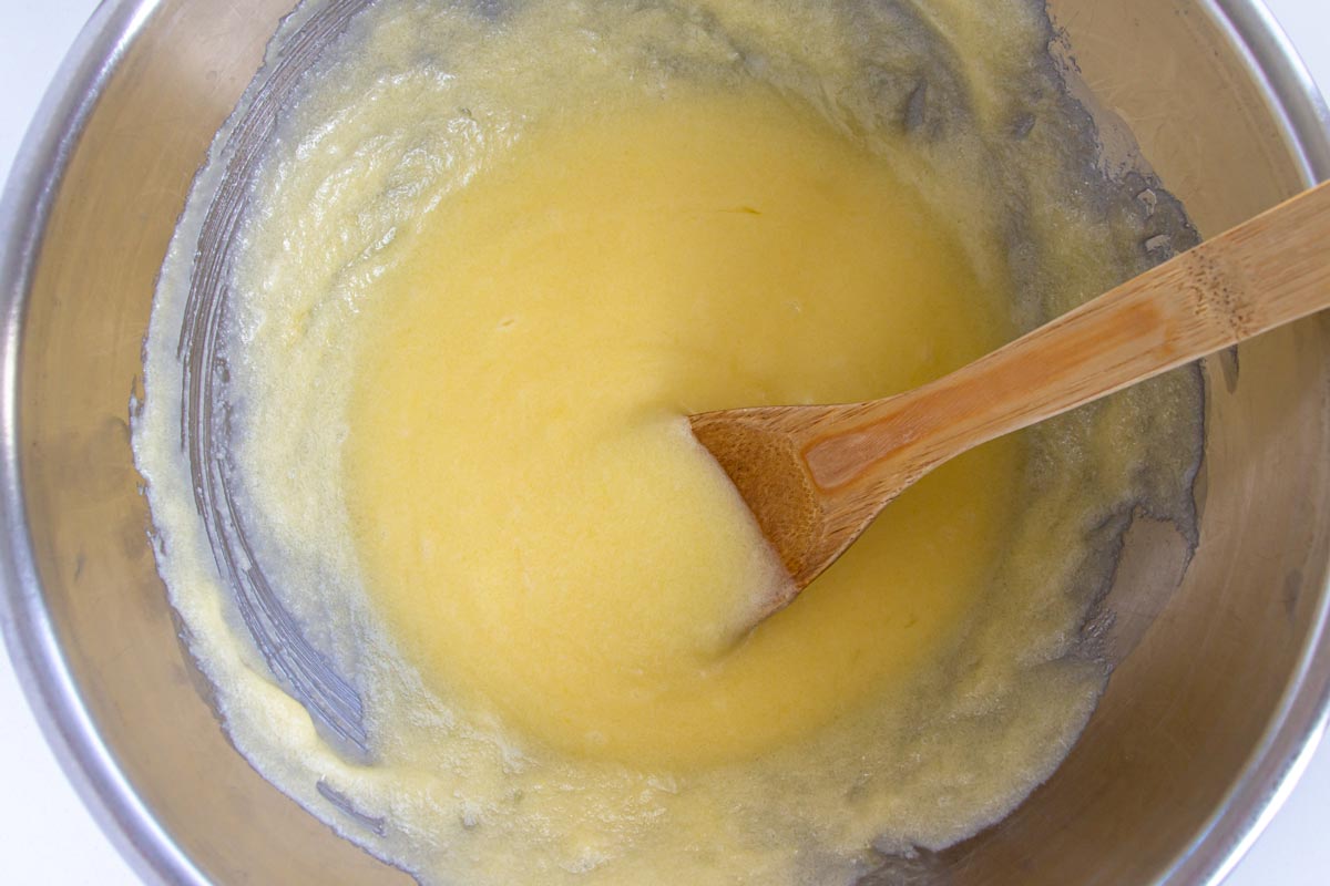 A mixture of butter, sugar, and eggs in a metal bowl with a wooden spoon.