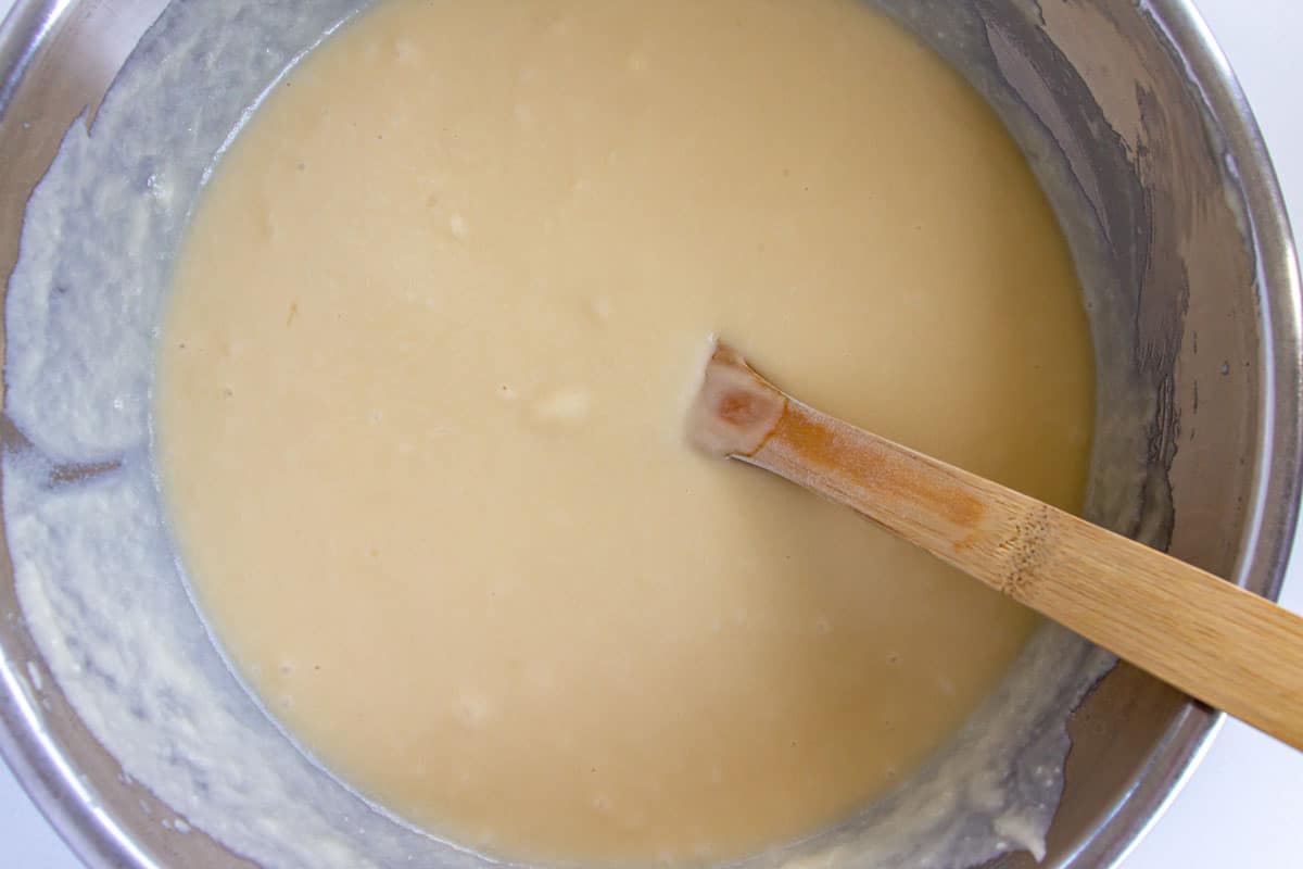A white batter in a metal mixing bowl with a wooden spoon.