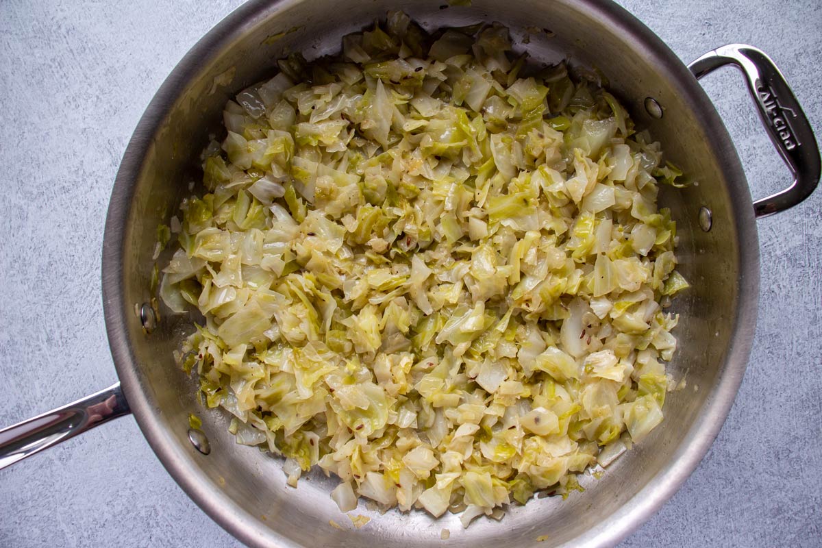 Cooked chopped green cabbage and onions in a stainless steel skillet.