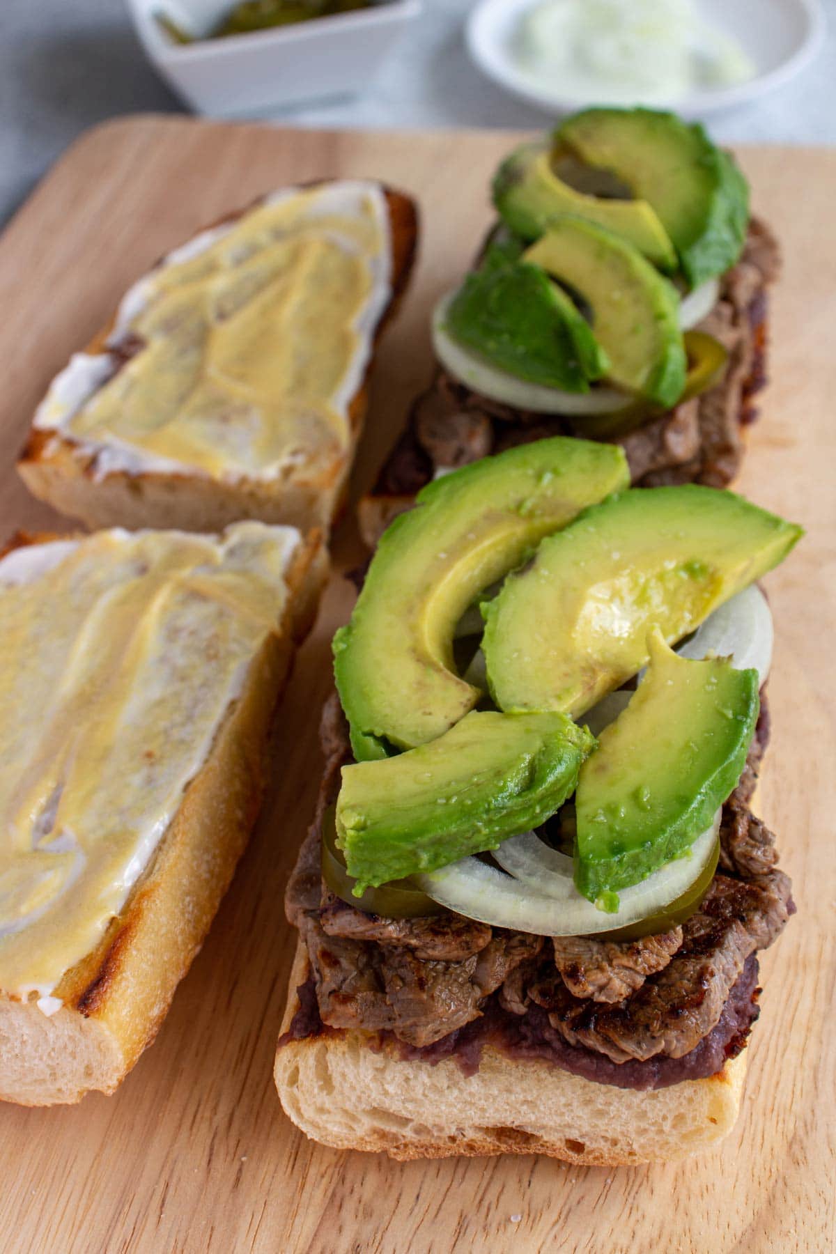 A baguette filled with steak, sliced onion and avocado with the bread lid on the side.