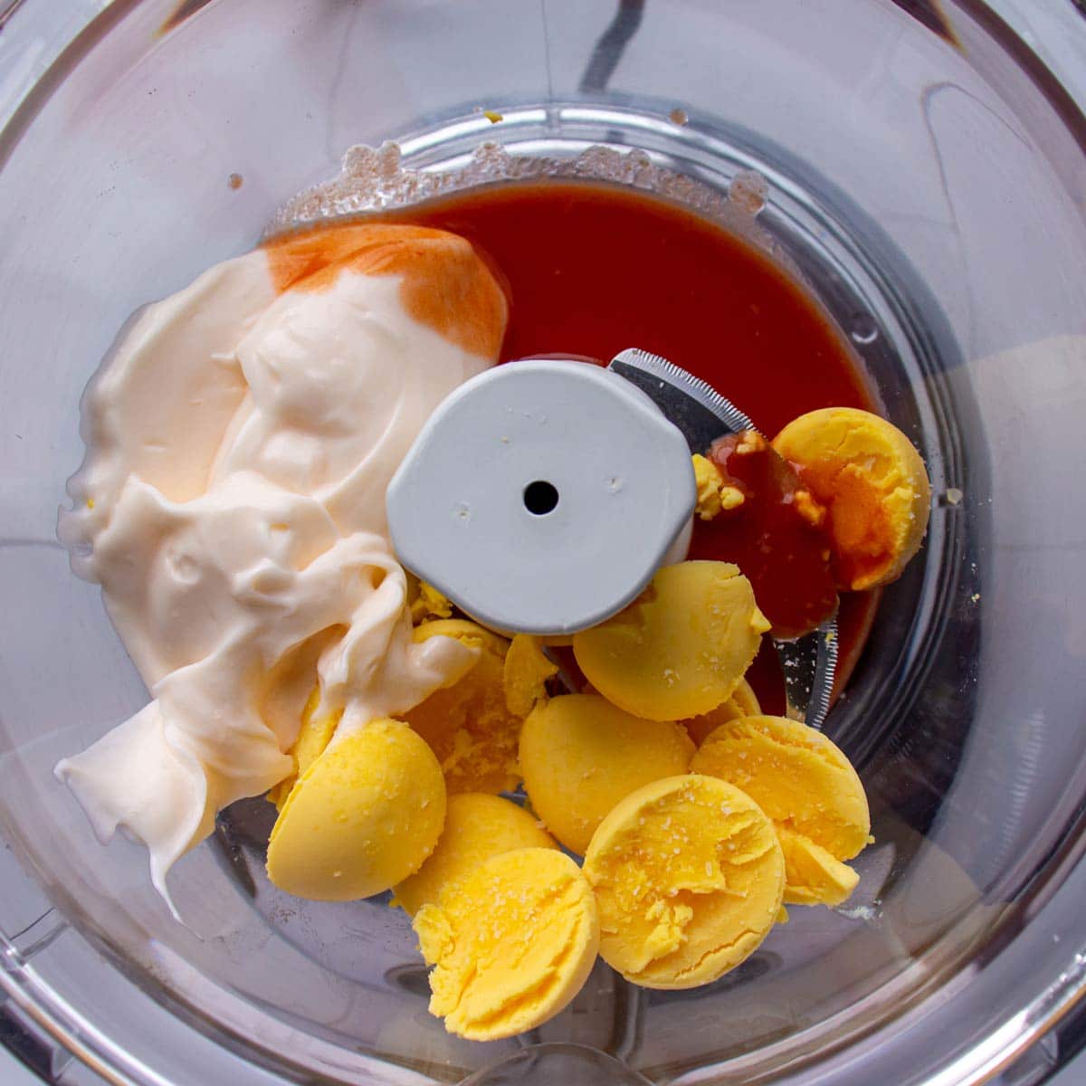 Hard-boiled egg yolks, mayonnaise, and hot sauce in the bowl of a food processor.