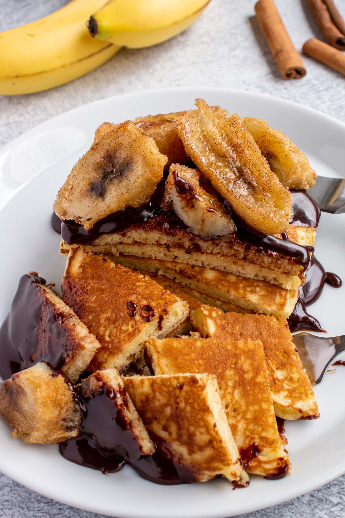 A stack of pancakes topped with chocolate sauce and fried crunchy bananas cut into large pieces.