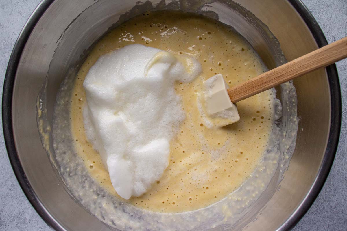 Batter in a metal mixing bowl with a large dollop of whipped egg whites on top.