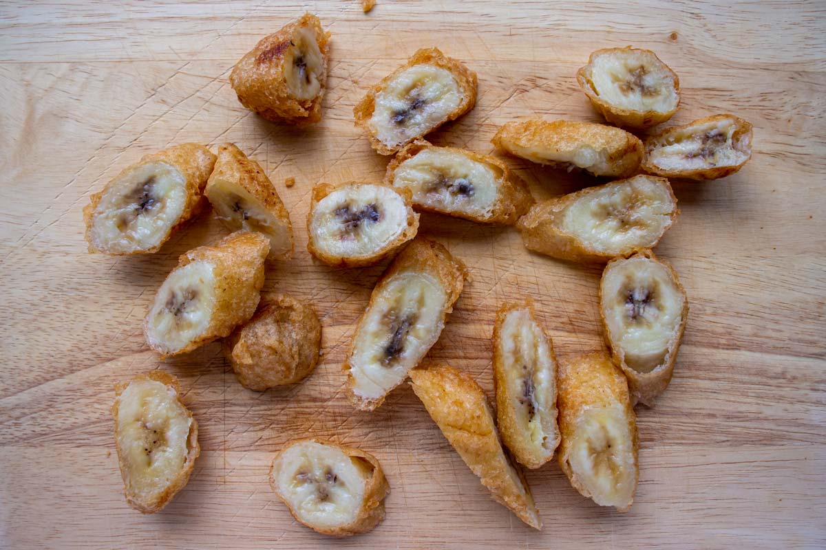 Battered and fried bananas sliced on the bias on a wooden board.