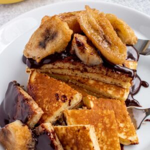 A stack of pancakes topped with chocolate sauce and fried crunchy bananas cut into large pieces.