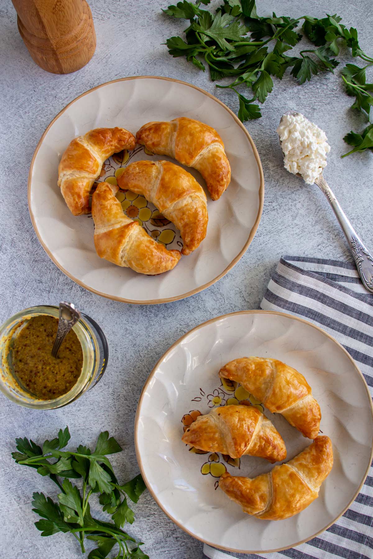 Two plates of ham croissants, parsley, a jar of mustard, and a spoon of quark cheese.