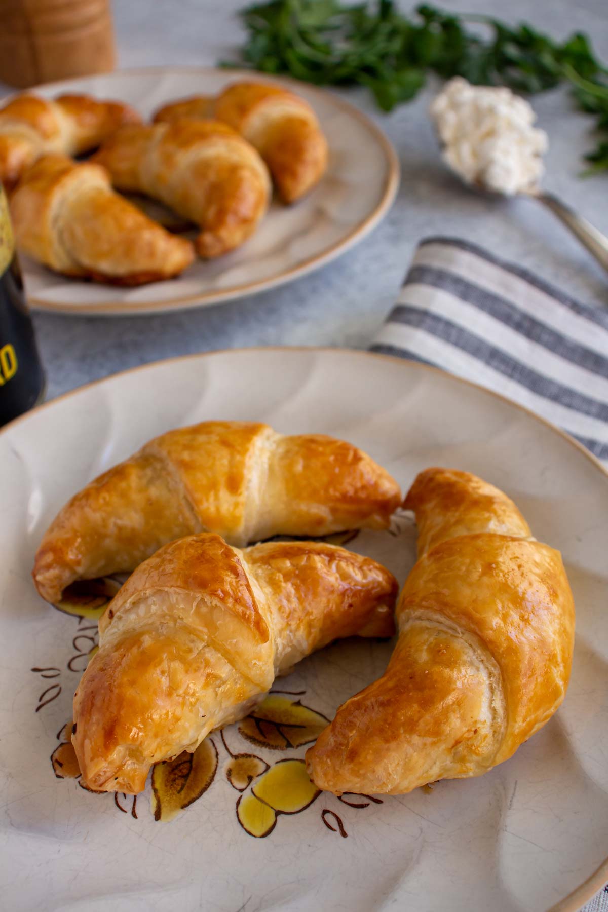 Closeup of three small golden brown ham croissants on a plate with more in the background.