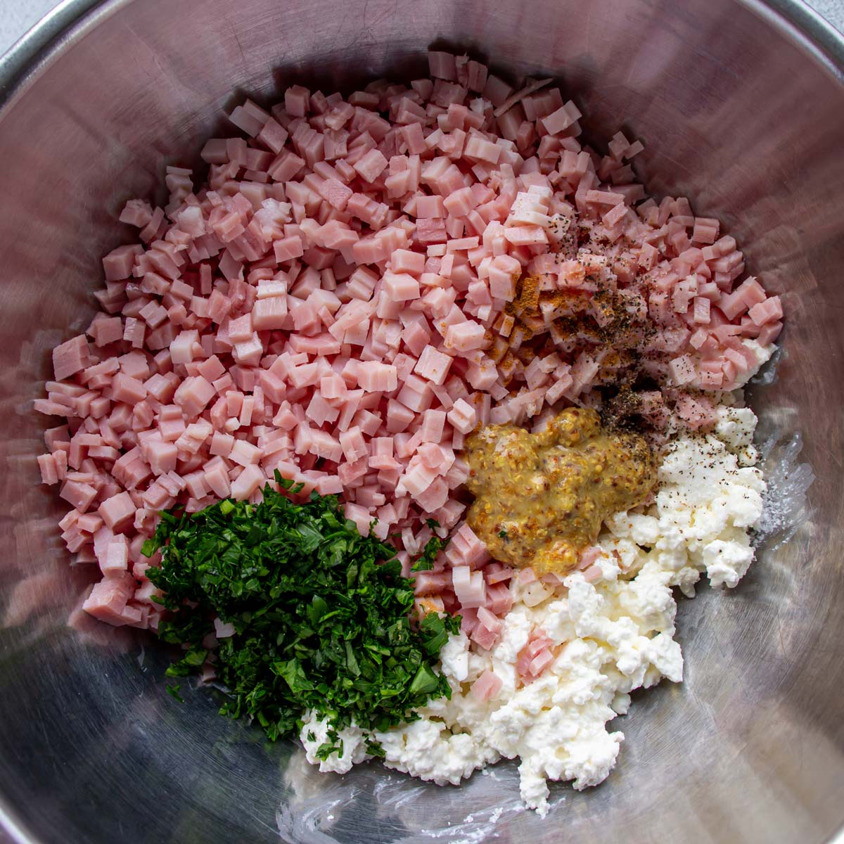 Chopped ham, parsley, coarse mustard, quark cheese, and seasonings in a metal mixing bowl.