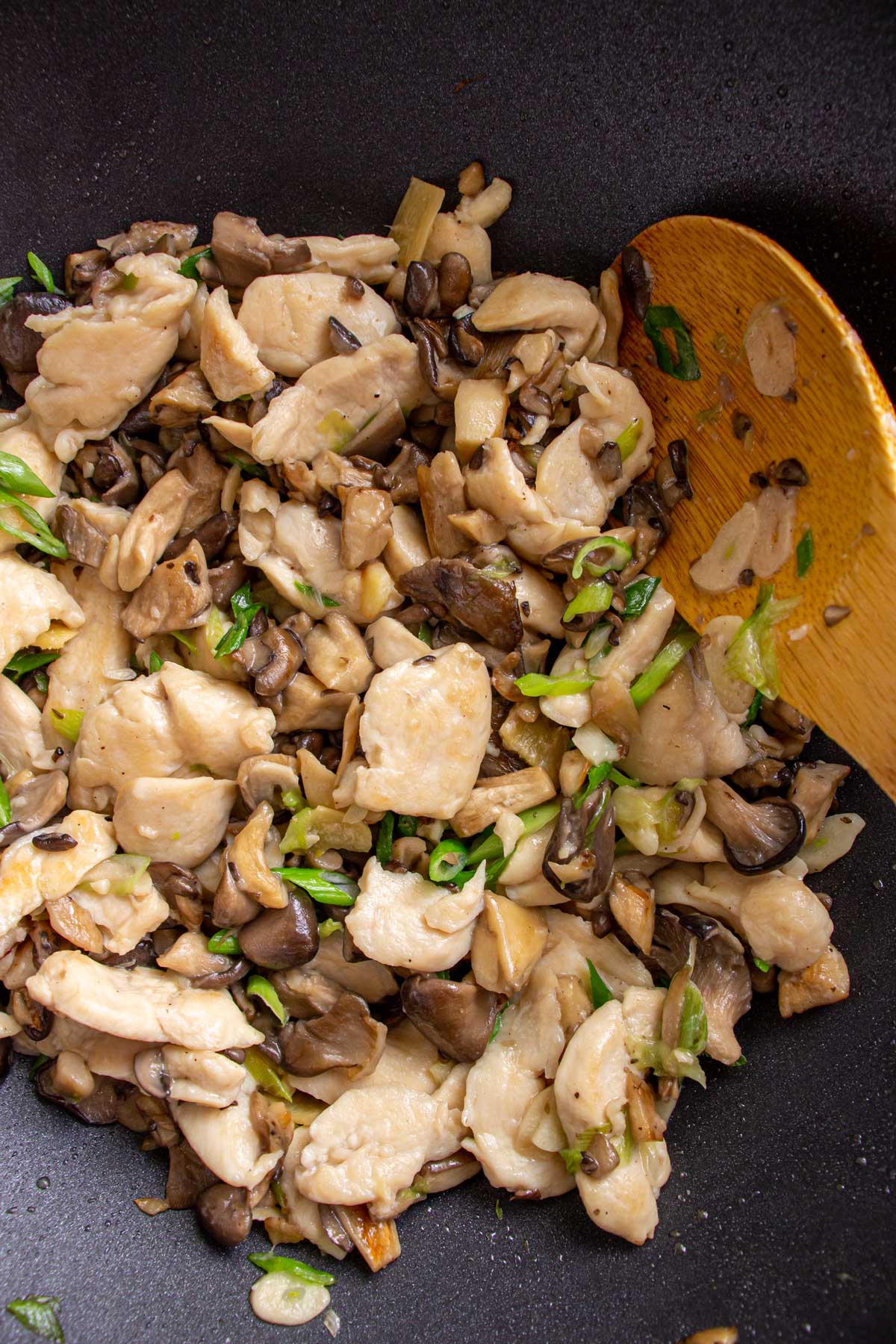 Closeup of stir-fried oyster mushrooms with chicken and scallions in a wok.