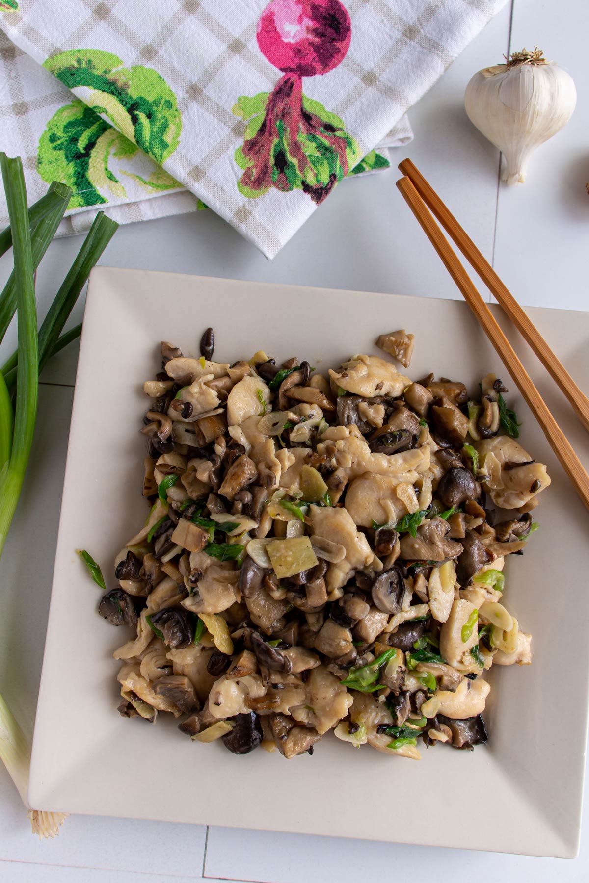 Chinese chicken and mushroom stir-fry on a square plate with chopsticks resting on the side.