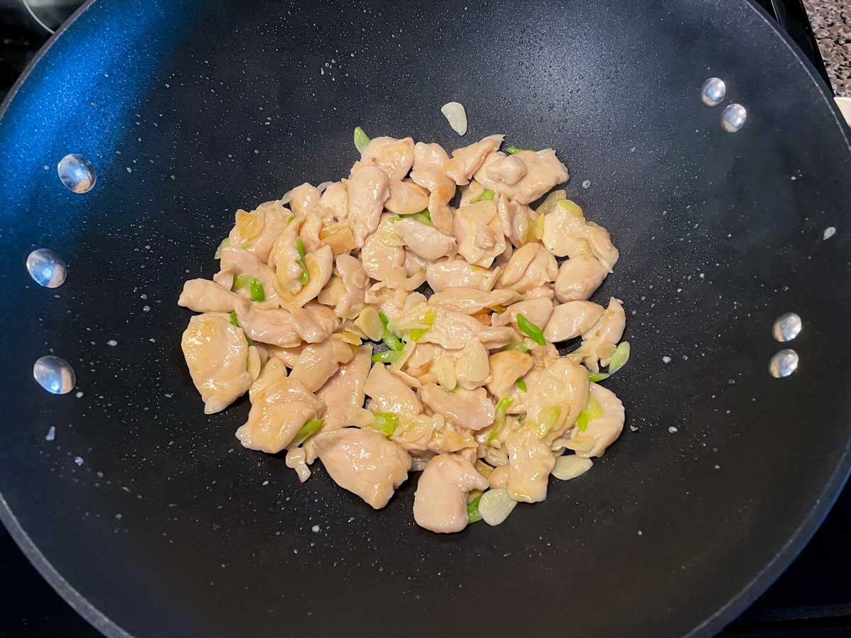 Stir-fried sliced chicken with garlic, ginger, and scallions in a wok.