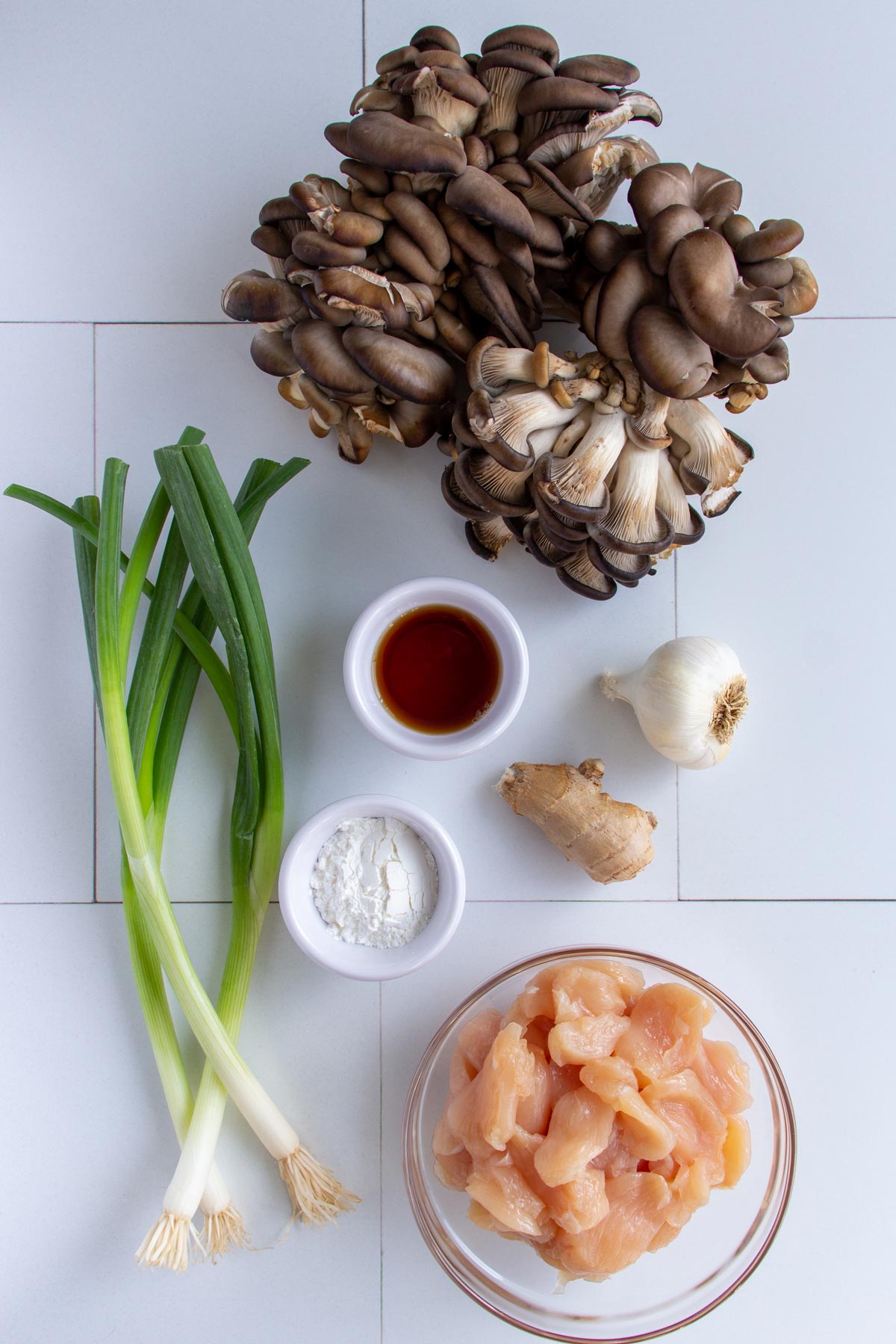 Ingredients for stir-fried oyster mushrooms with chicken on a white tile background.