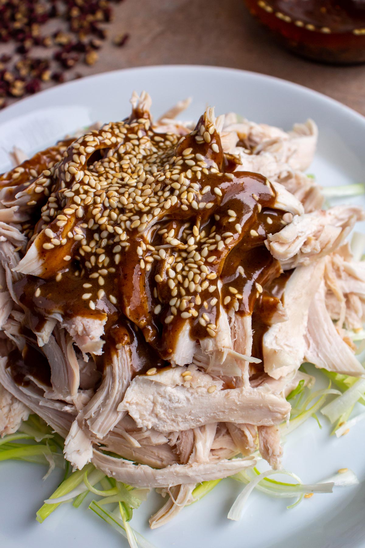 Closeup of shredded chicken with strange flavor sauce and sesame seeds on a bed of scallion slivers.