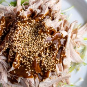 Closeup of strange flavor chicken with dark brown sauce and sesame seeds on a white plate.